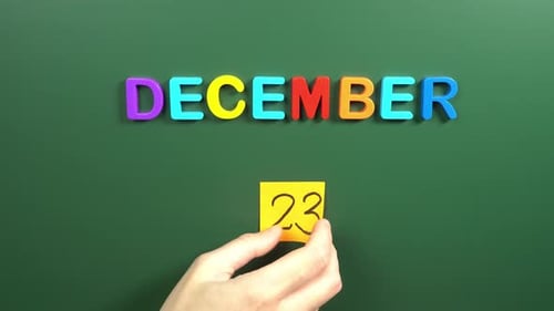 Hand sticking a sticker 23 December calendar day on school board. 23 date of December. Twenty third