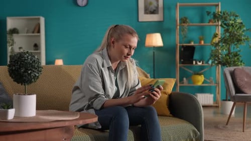 A Woman Using a Smartphone While Sitting on the Sofa at Home Close Up A Woman Looks Through Social