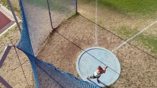 High angle: Young woman athlete throws discus on grass sports field