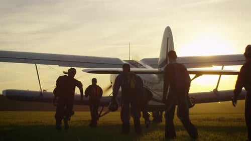 Group Approaches Airplane on Field at Sunset