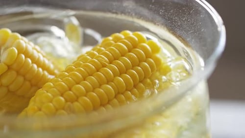 Sweet tasty boiled corn is boiling in a saucepan. Close-up of bubbles hot air when boiling come out