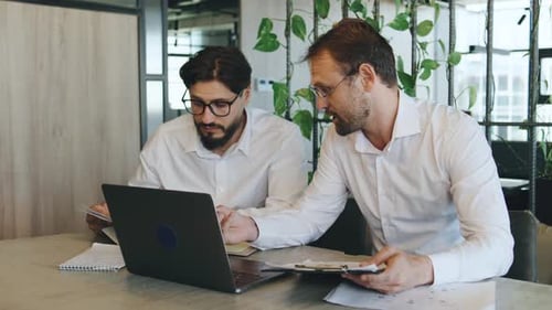 Business Meeting Between Two Men in a Modern Office Discussing Project Details While Using a Laptop