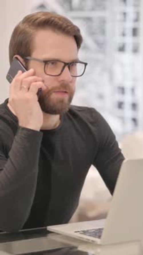 Man with beard talking on phone at desk