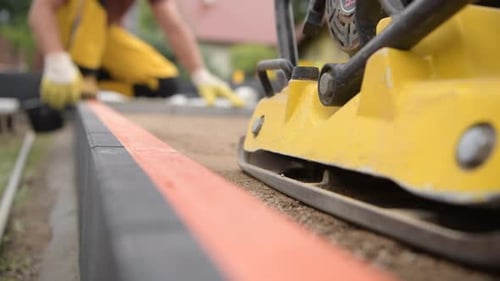 Travailleur équipé d'un compacteur de sol préparant le terrain pour le pavage