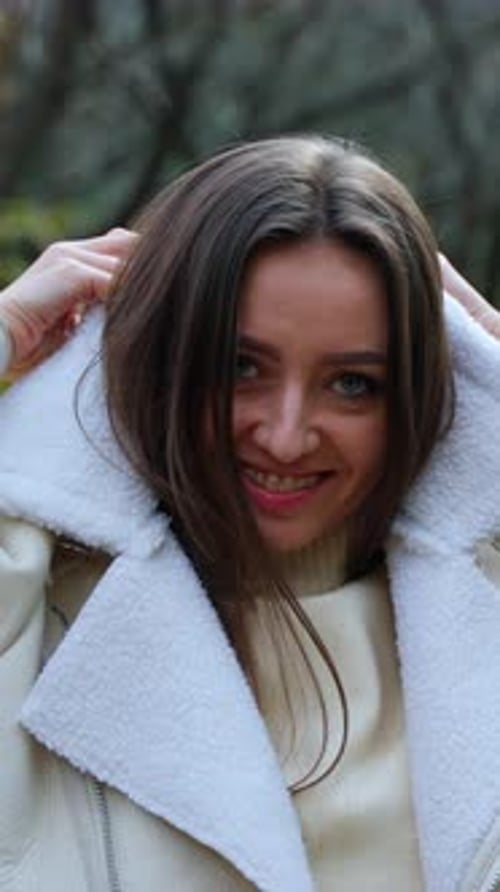 Cheerful positive lady puts on warm jacket walking in the park.
