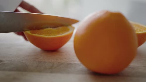 CloseUp of a Hand Cutting Fresh Oranges on a Wooden Surface