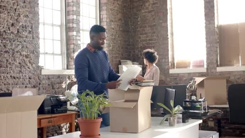 Diverse colleagues unpacking boxes with documents and office items in creative office in slow motion