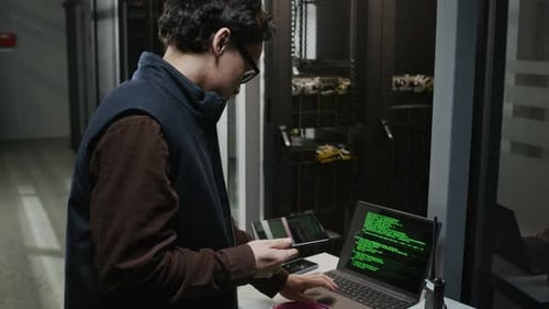 Network Engineer Using Tablet and Laptop with Green Code in Data Center