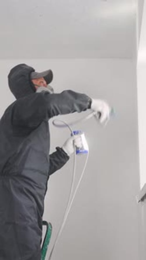 Painter Builder Worker Paints with an Airless Sprayer A Painter Professionally Paints a Wall with a