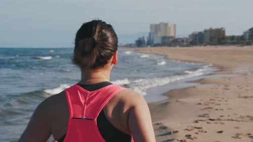 Back follow shot of woman running on beach.