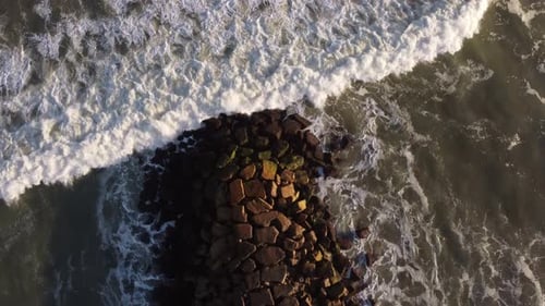 Aerial top down shot of stormy waves of ocean crashing against rocky jetty during sunset - Circle sh