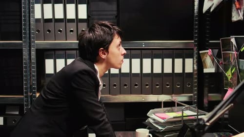 Woman in Suit Leans on Desk in Office