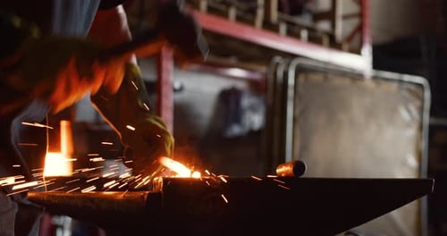 Young male blacksmith hammering hot metal in a softly lit workshop