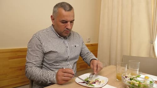 55A man is eating a salad while sitting at a table. Close-up.