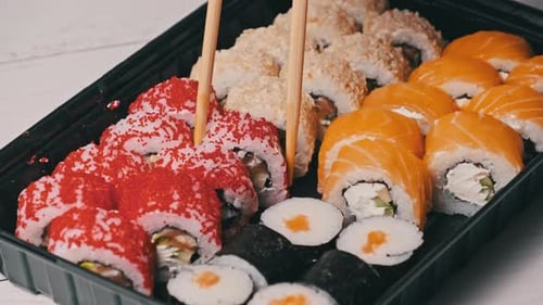 Sticks Take Sushi From the Plastic Sushi Box CloseUp