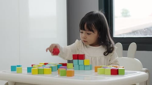 toddler girl playing block toy to stacks building cubes on a table