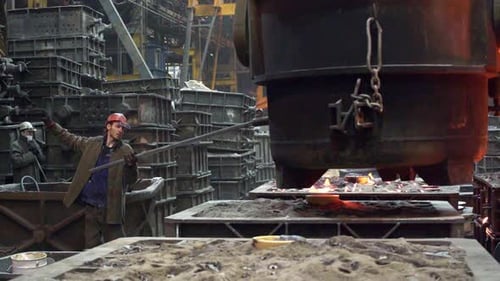An Industrial Worker Skillfully Managing the Flow of Molten Metal in a Bustling Foundry Stock Clip