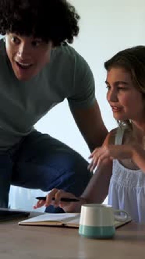 Vertical video: Couple receiving paper at wooden table, writing notes and tapping tablet for study