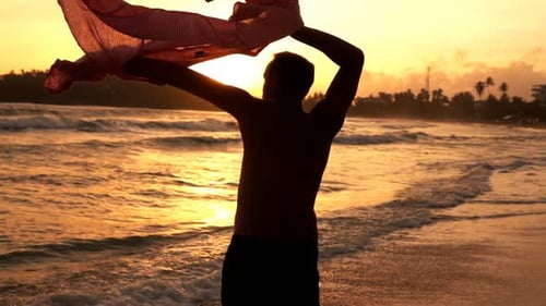 Silhouette of Man Putting on Shirt on Beach During Sunset Super Slow