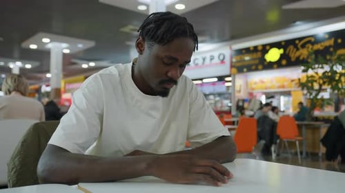 Thoughtful Man Sitting Alone At Table In Indoor Eatery With Busy Background