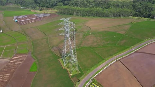 Flyover rice field with high voltage electricity tower on the middle of it - Orbit drone shot