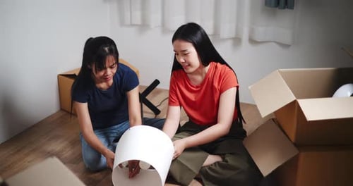 Two Asian siblings sit on the floor and help assemble a floor lamp in their new home.