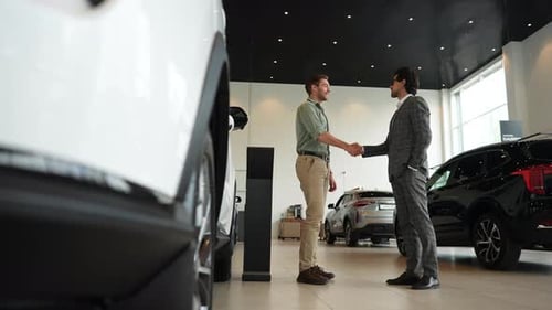 Blick aus der Vogelperspektive auf einen selbstbewussten Autoverkäufer im Geschäftsanzug und einen fröhlichen männlichen Kunden im Auto