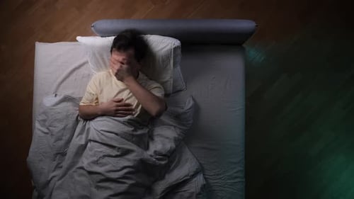 Man Lying Awake in Bed at Night Clutching His Head in Frustration Drained By Insomnia and Anxiety