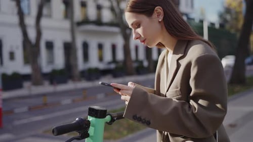 Woman Uses Phone by Electric Scooter on Street