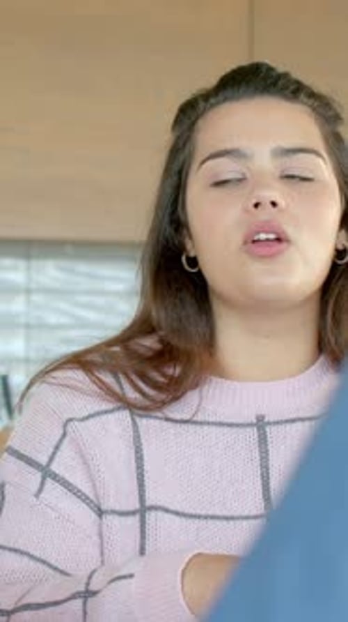 Vidéo verticale : partenaire repérant une femme en haut rose avec un chouchou, parlant, penchée à la table de la cuisine