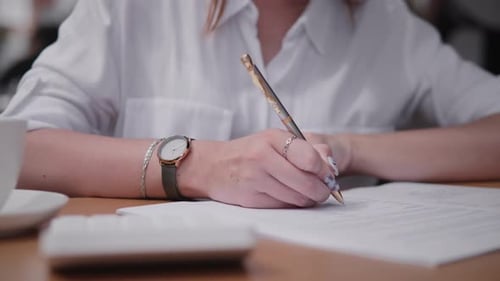 Woman Writes on Paper at Desk With Pen