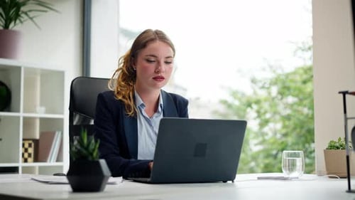 in a Modern Office with a Large Window a Beautiful Worker in a Blue Shirt with a Laptop Looks at the