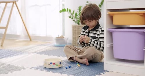 Little Boy Stringing Colorful Beads at Home