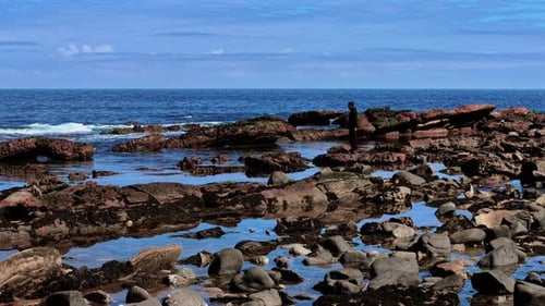 Young Man Standing on Rocks By Ocean Shore Teenager Watching Waves From Rugged Coastal Stones