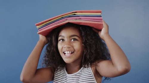 Happy Girl Balancing Books on Head Against Blue Backdrop