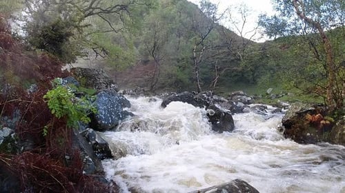 Slow motion rocky flowing woodland waterfall river water splashing on riverbank rock formation