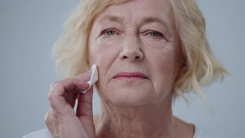 Senior woman cleaning face with cotton pad close-up