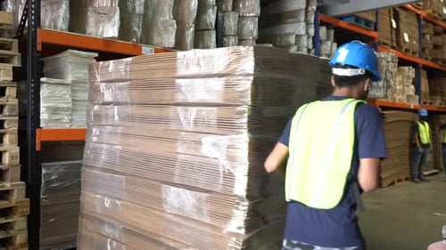 Un travailleur de sexe masculin à l'intérieur d'un entrepôt déplace une palette chargée de boîtes en carton sur son axe et se déplace
