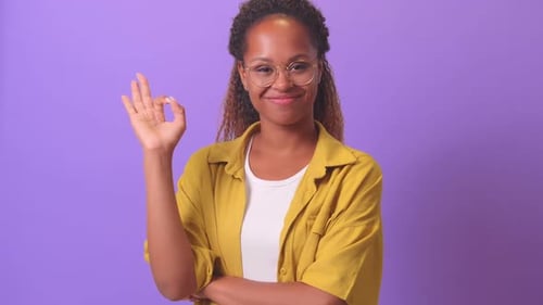 Jovem mulher afro-americana sorridente e bonita faz um gesto OK em pé no estúdio