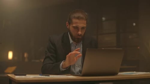 Portrait of Serious Attractive Businessman Sit at Desk Working Use Laptop at Night Office