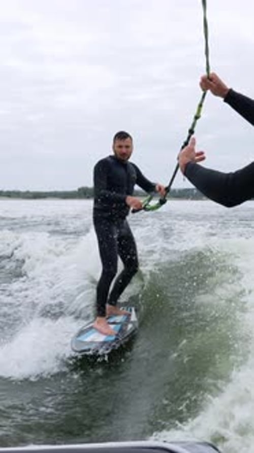 Man wake surfing on lake, another man holds rope