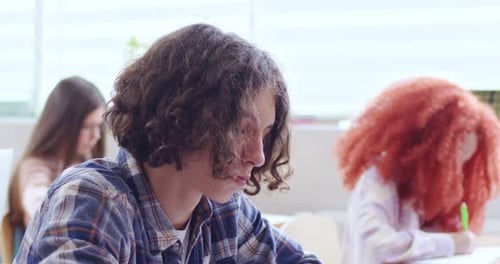 Close Up of Pensive Boy with Curly Hairstyle Studying in Classroom with Classmates at Elementary