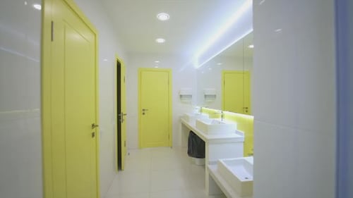 Washroom in white and yellow colors. Contemporary water closet with clean sinks in hospital.