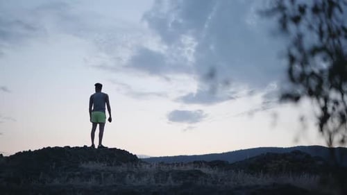 Epic twilight view of man standing on mountain peak, raising hands