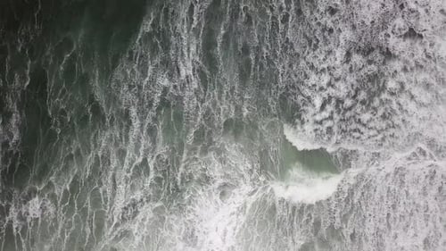 Stormy sea with waves breaking, white foam and beach sand dragged into the sea
