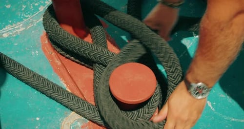 Nahaufnahme einer Seemannshand, die ein Boot mit einem Seil an einer Klampe befestigt. Die fokussierte Aktion zeigt Erfahrung an