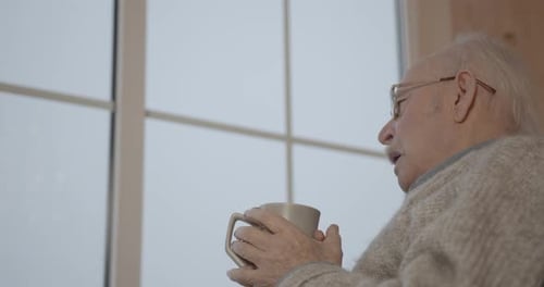 Old Man in Wheelchair Drinking Tea Near Window