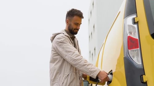 A Man Unplugs Charging Cable Electric Vehicle Near Warehouse