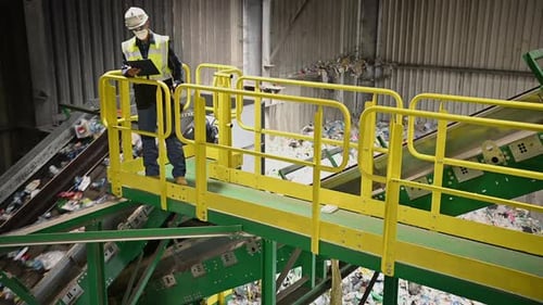 Worker Inspecting Recycling Conveyor System in a Waste Processing Facility