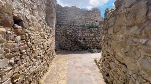 A narrow stone pathway surrounded by ancient, weathered walls, leading through the ruins